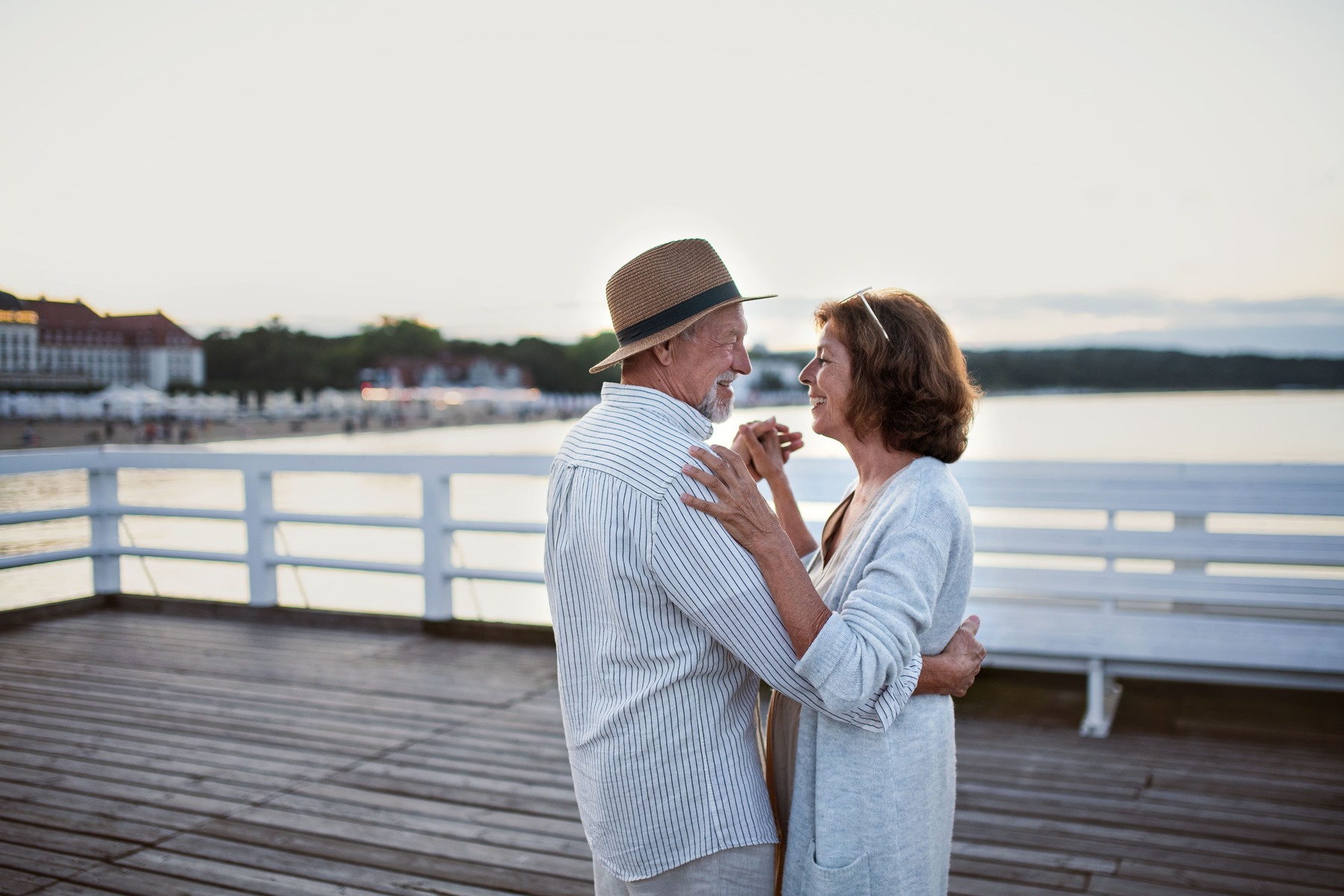 Feliz pareja senior enamorada bailando al aire libre en el muelle junto al mar, mirándose el uno al otro