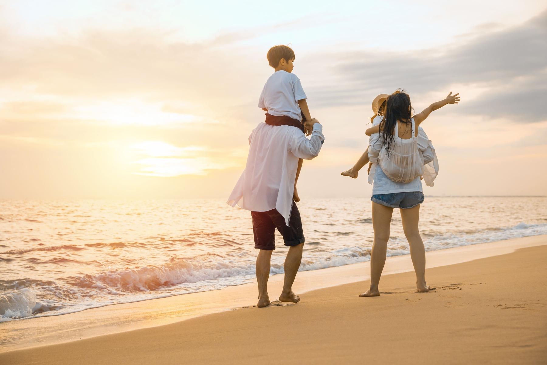 Padres con niños en hombros en la playa al atardecer