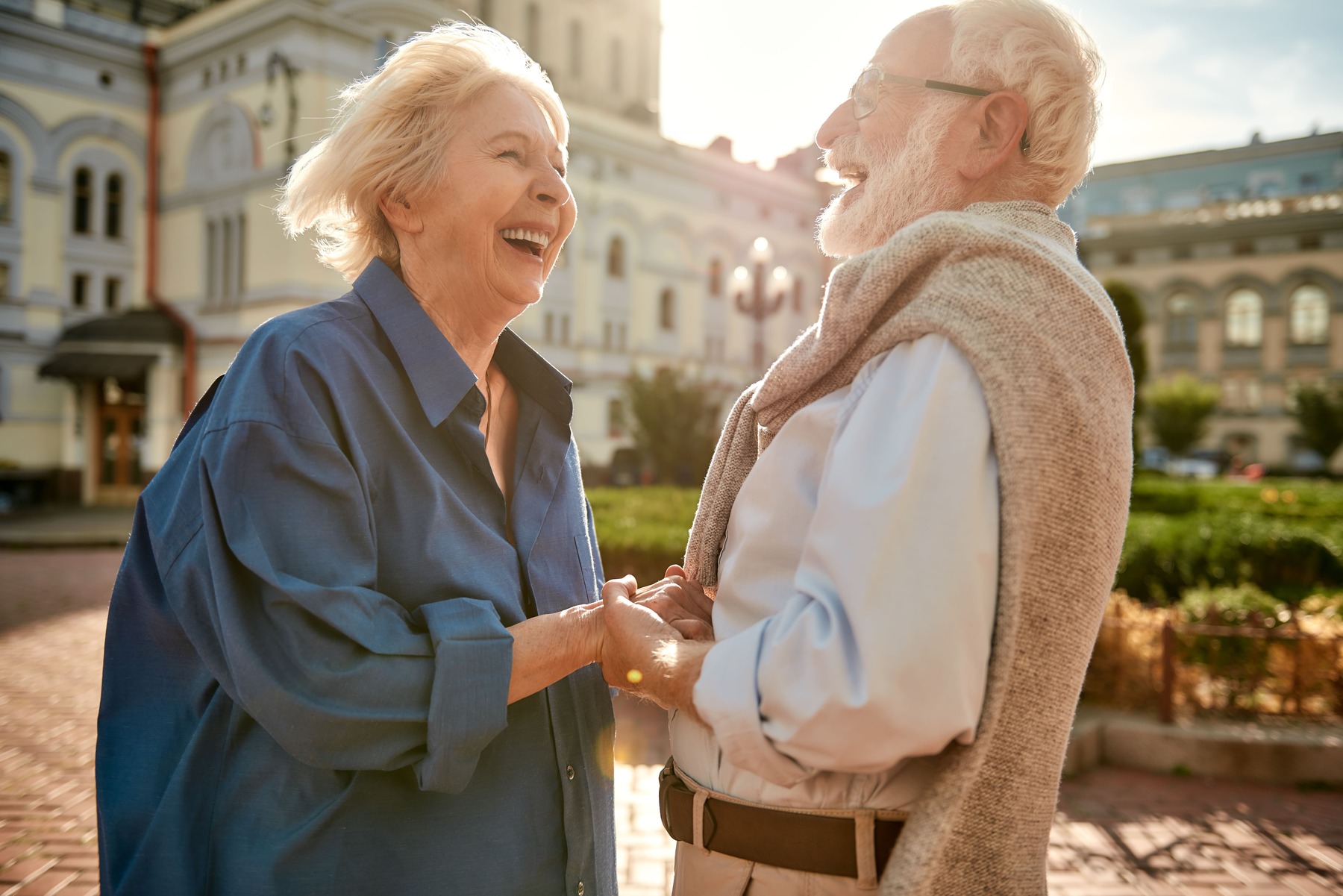 Feliz pareja de ancianos tomados de la mano y riendo mientras están de pie